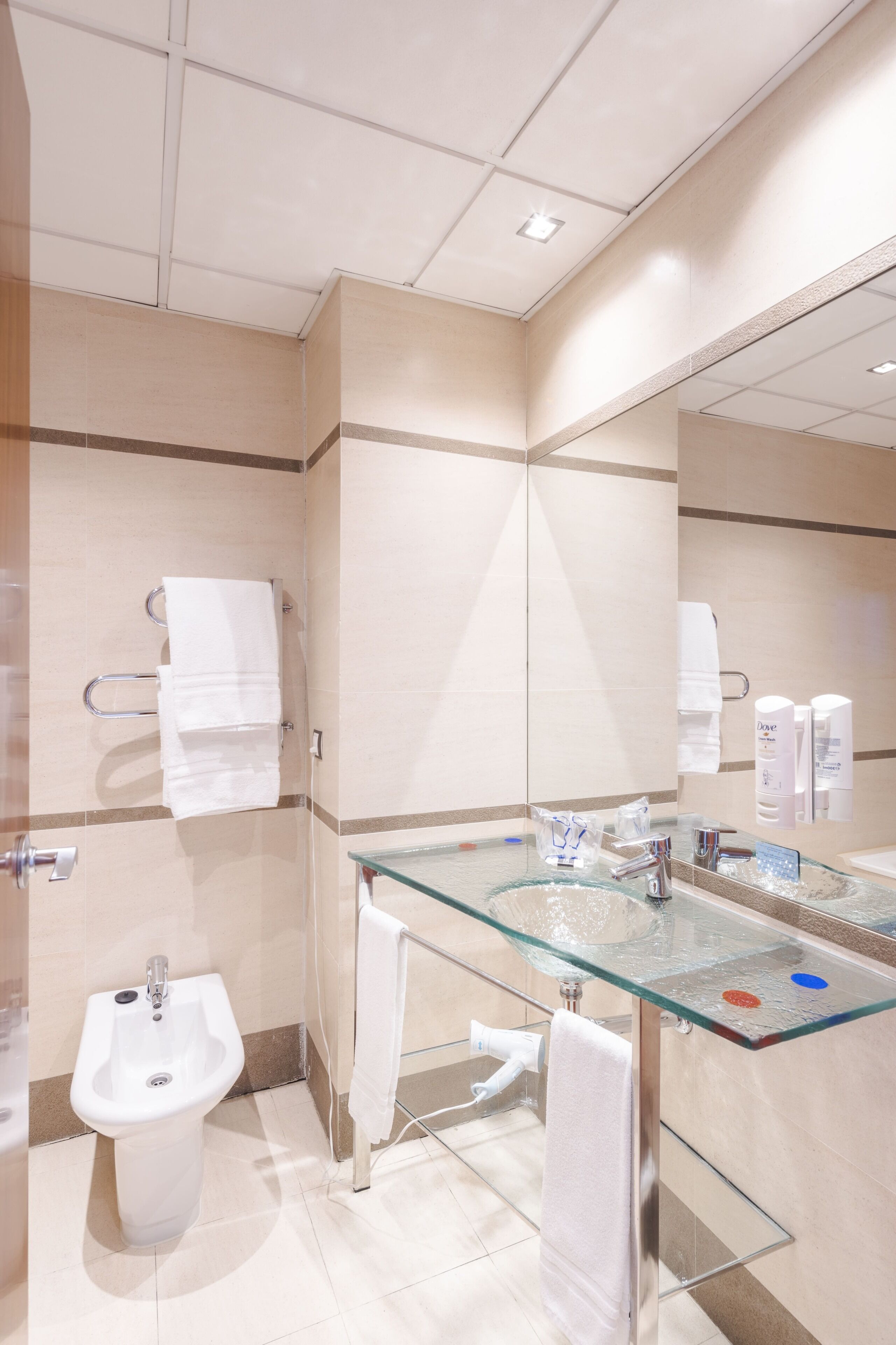 Un baño moderno con un lavabo de vidrio, un bidé y un espejo grande.