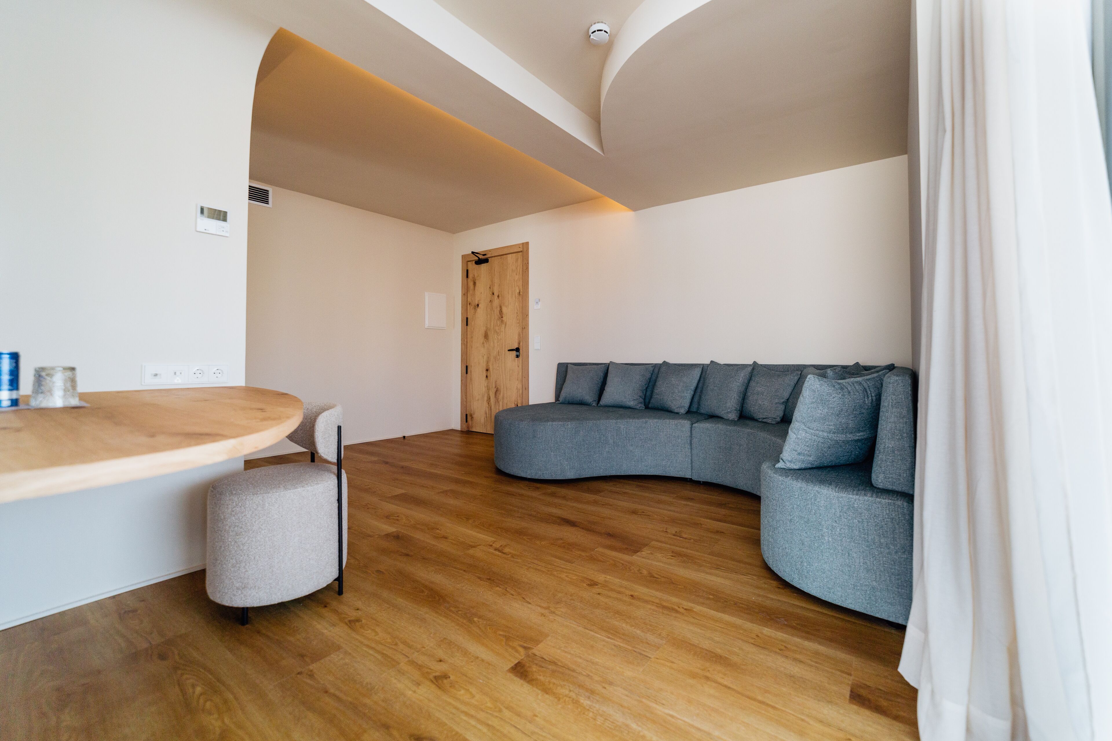 Un salon moderne avec un canapé gris aux lignes courbes, une table basse en bois et un petit pouf gris.