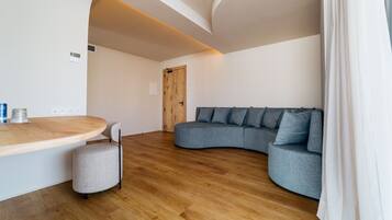 Un salon moderne avec un canapé gris aux lignes courbes, une table basse en bois et un petit pouf gris.