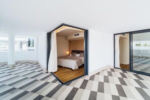 Una habitación de hotel moderna con piso a cuadros, una cama con cabecera y un amplio ventanal corredero que da a un balcón.
