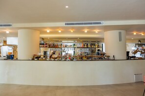 Una zona de bar con mostrador, estantes llenos de botellas y diversos utensilios.
