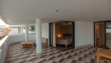 A hotel balcony with a checkered floor, a sofa, a wooden table, and a bed visible through an open door.