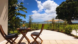 A patio with two wooden chairs and a table, overlooking a beach and a large tree. - The Sands Hotel (Omapere)