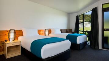 Een hotelkamer met twee bedden, een nachtkastje, een lamp en uitzicht op het omliggende landschap.