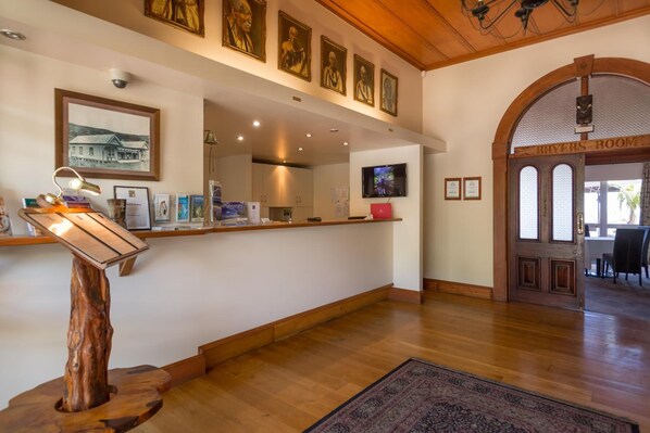 A reception area with a wooden desk, framed artwork on the wall, and a sign for the Bryers Room. - The Sands Hotel (Omapere)