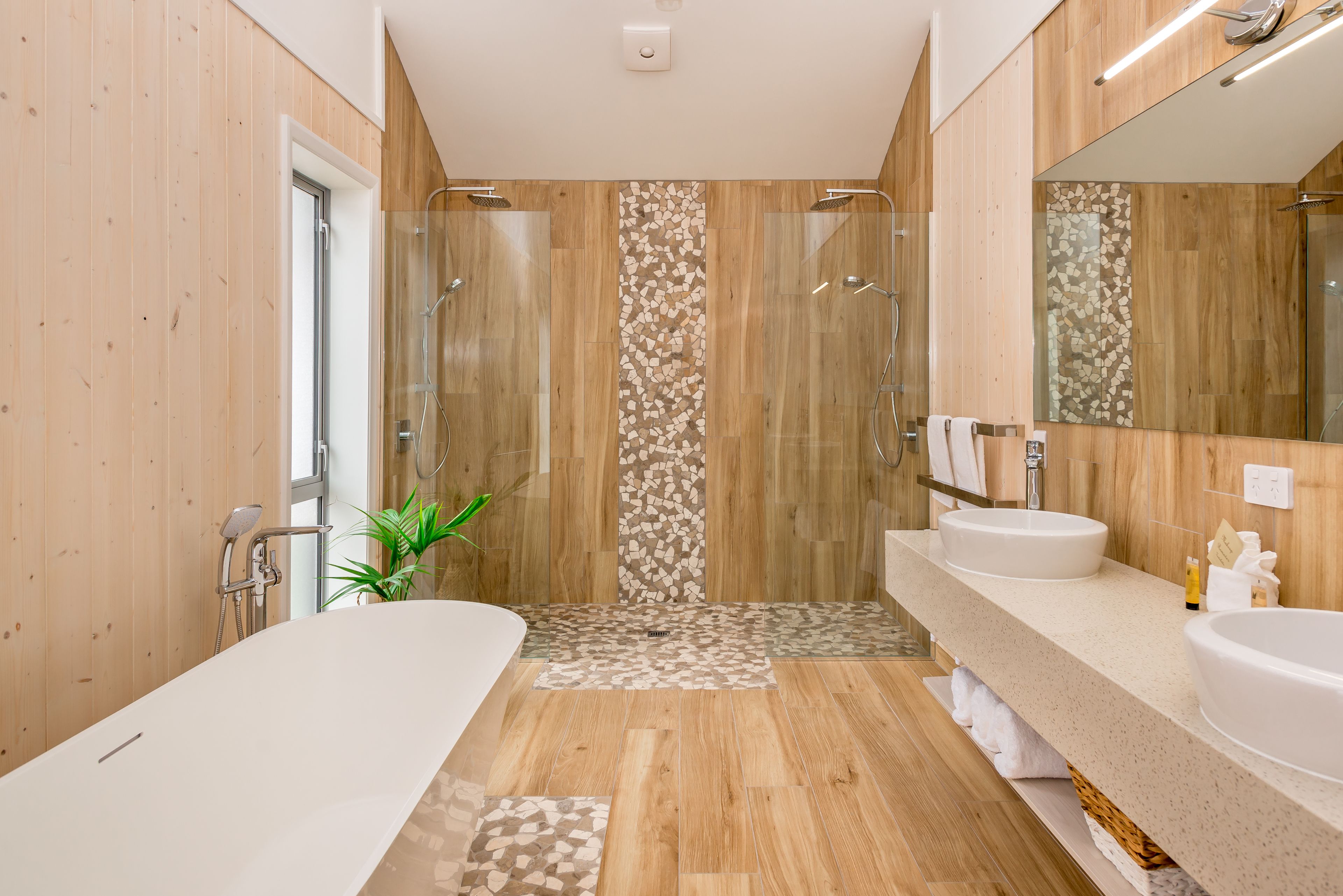 A modern bathroom with a wooden floor, two sinks, a large mirror, and a shower area.