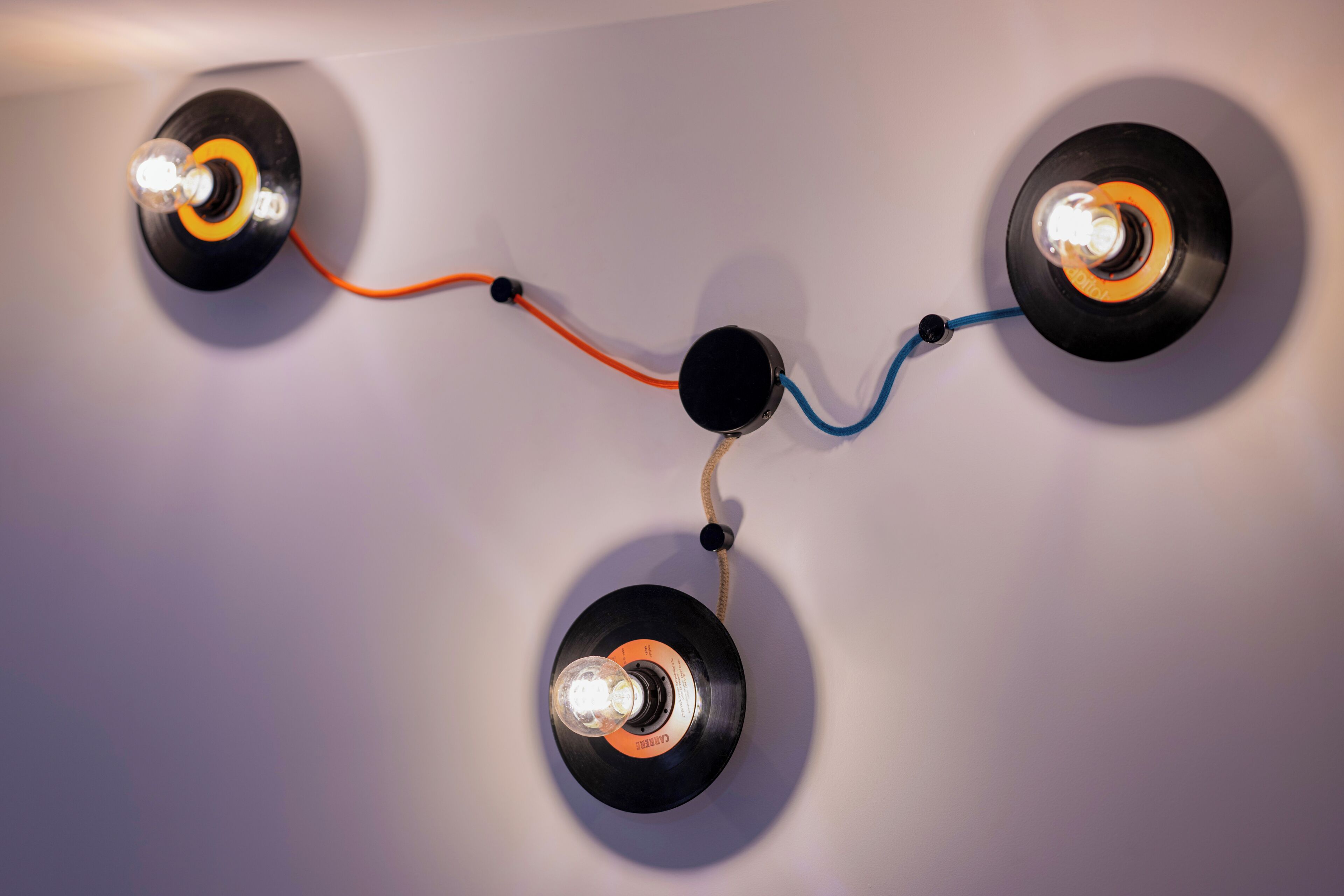 A wall-mounted lighting fixture with three vinyl records as light sources, connected by wires.
