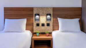 Une chambre d’hôtel avec deux lits, une tête de lit en bois, des lampes fixées au mur et deux petites plantes en pot posées sur une table de chevet.
