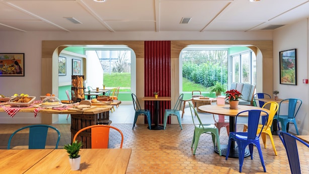Un espace repas doté d’un sol à motifs hexagonaux, de chaises colorées et d’une table dressée avec de la nourriture et des boissons.