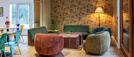 A cozy room with a patterned wallpaper, a green sofa, a red armchair, and a small table with a lamp.