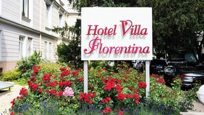 Une enseigne indiquant l’hôtel Villa Florentina, entourée d’un jardin agrémenté de fleurs rouges et violettes.