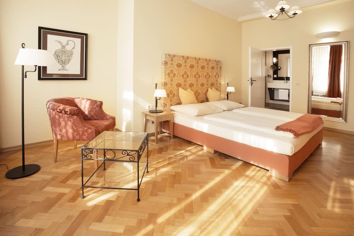 Quarto de hotel com cama, poltrona, mesa, luminária e um quadro na parede.