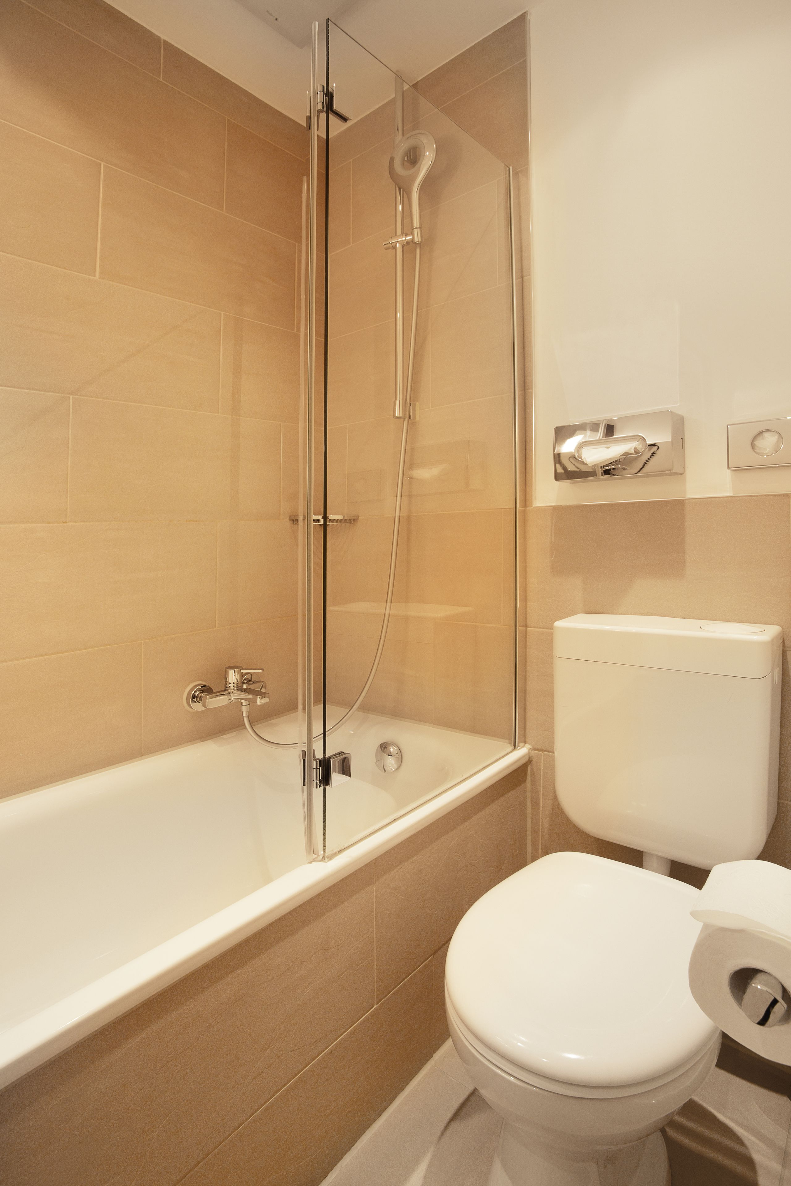 A bathroom with a glass-enclosed shower, a white toilet, and beige tiles.