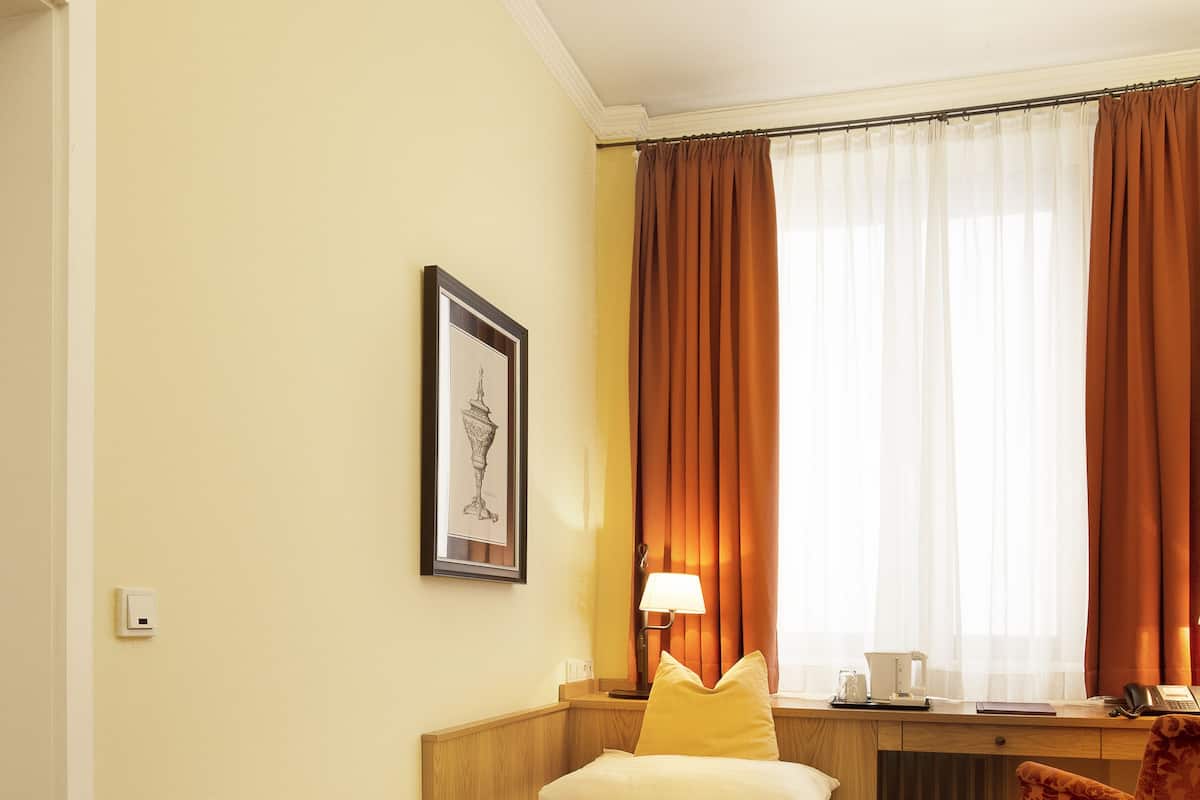 Quarto de hotel com cama, escrivaninha, cadeira e janela com cortinas.
