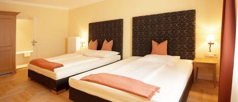 A hotel room with two beds, wooden flooring, and a wardrobe.