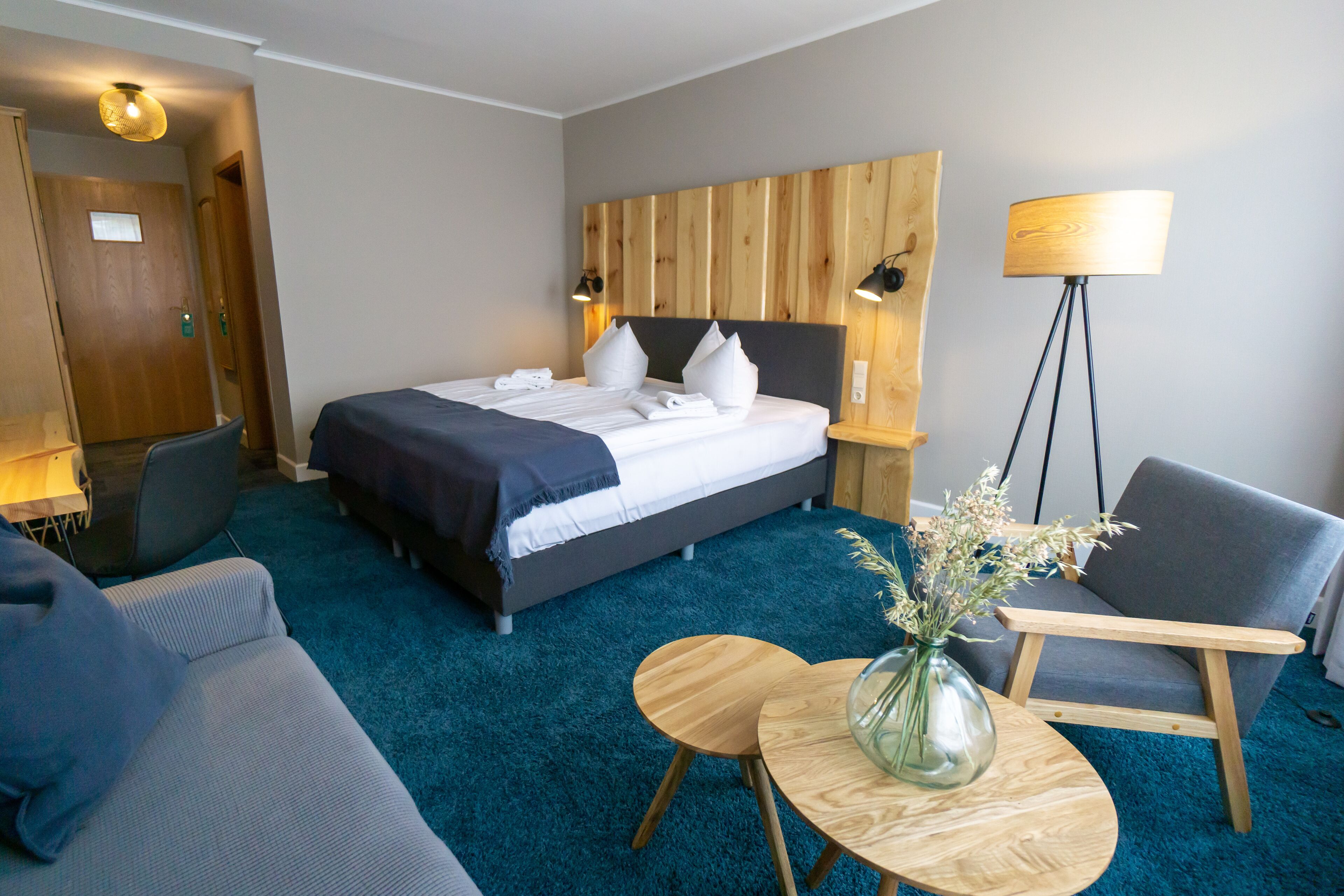 A hotel room with a bed, a desk, a chair, a lamp, and a vase with flowers.