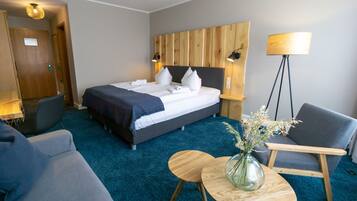 A hotel room with a bed, a desk, a chair, a lamp, and a vase with flowers.