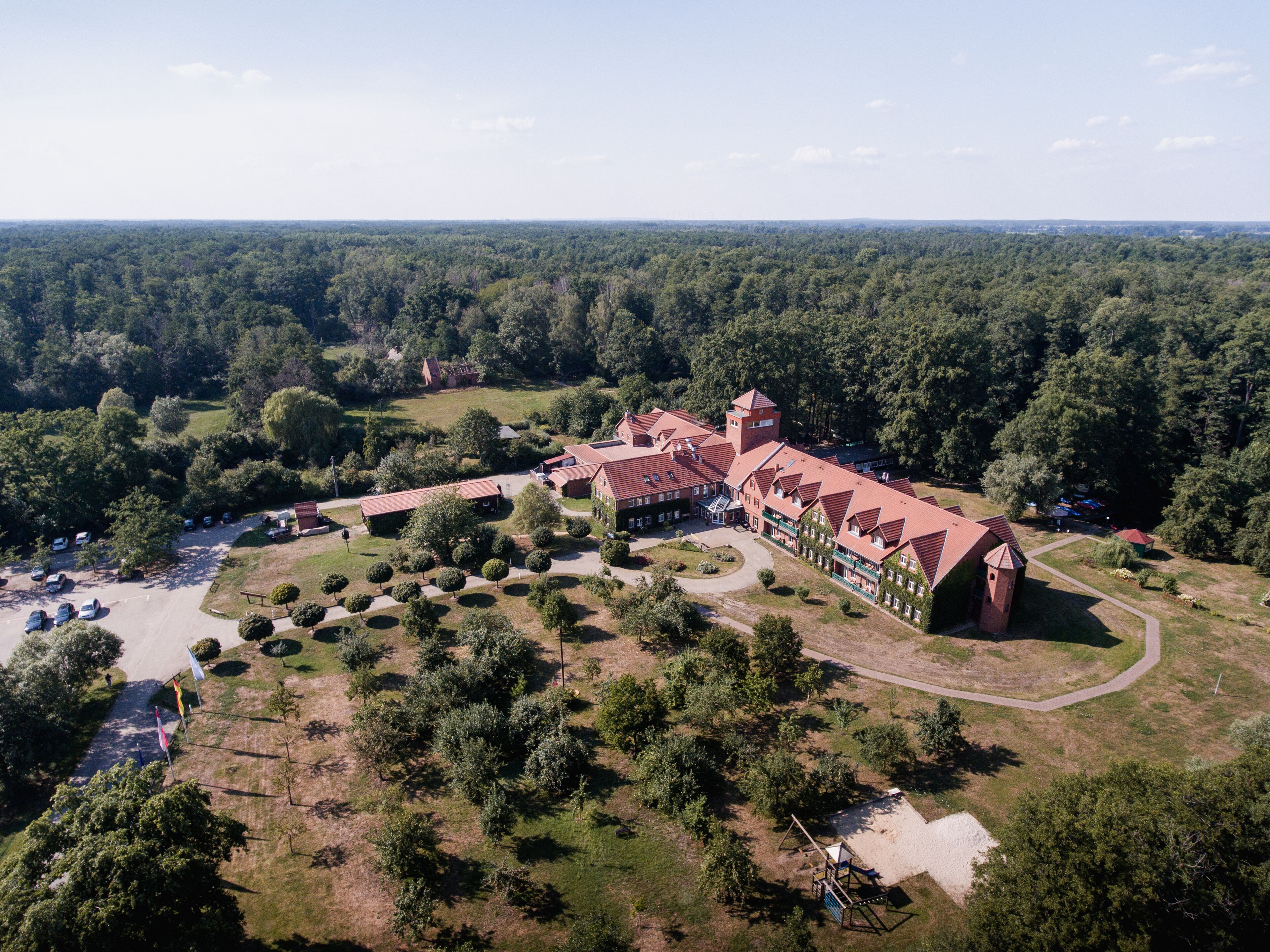 A large, red-roofed building with multiple wings, surrounded by a forested area.