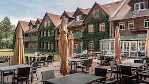 A patio area with outdoor seating and umbrellas, a brick building with green ivy, and a clear sky.