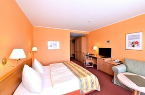 A hotel room with a bed, desk, chair, television, and a small table. - Waldhotel Eiche (Lübbenau/Spreewald)