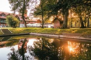 A serene outdoor setting with a reflective pond, a wooden deck, and a building with a red roof.