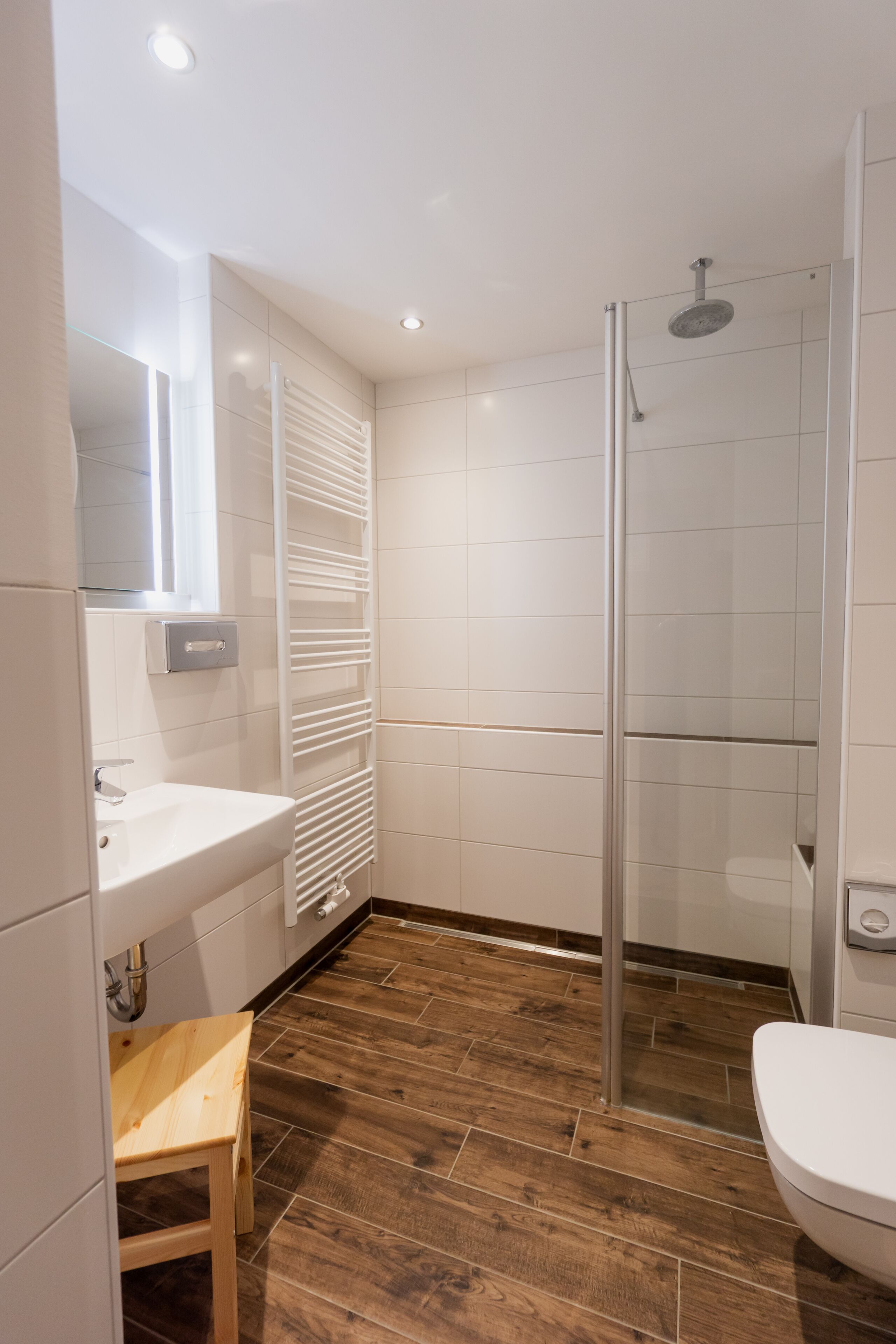 Une salle de bain moderne avec une douche à parois de verre, un banc en bois et un lavabo blanc.