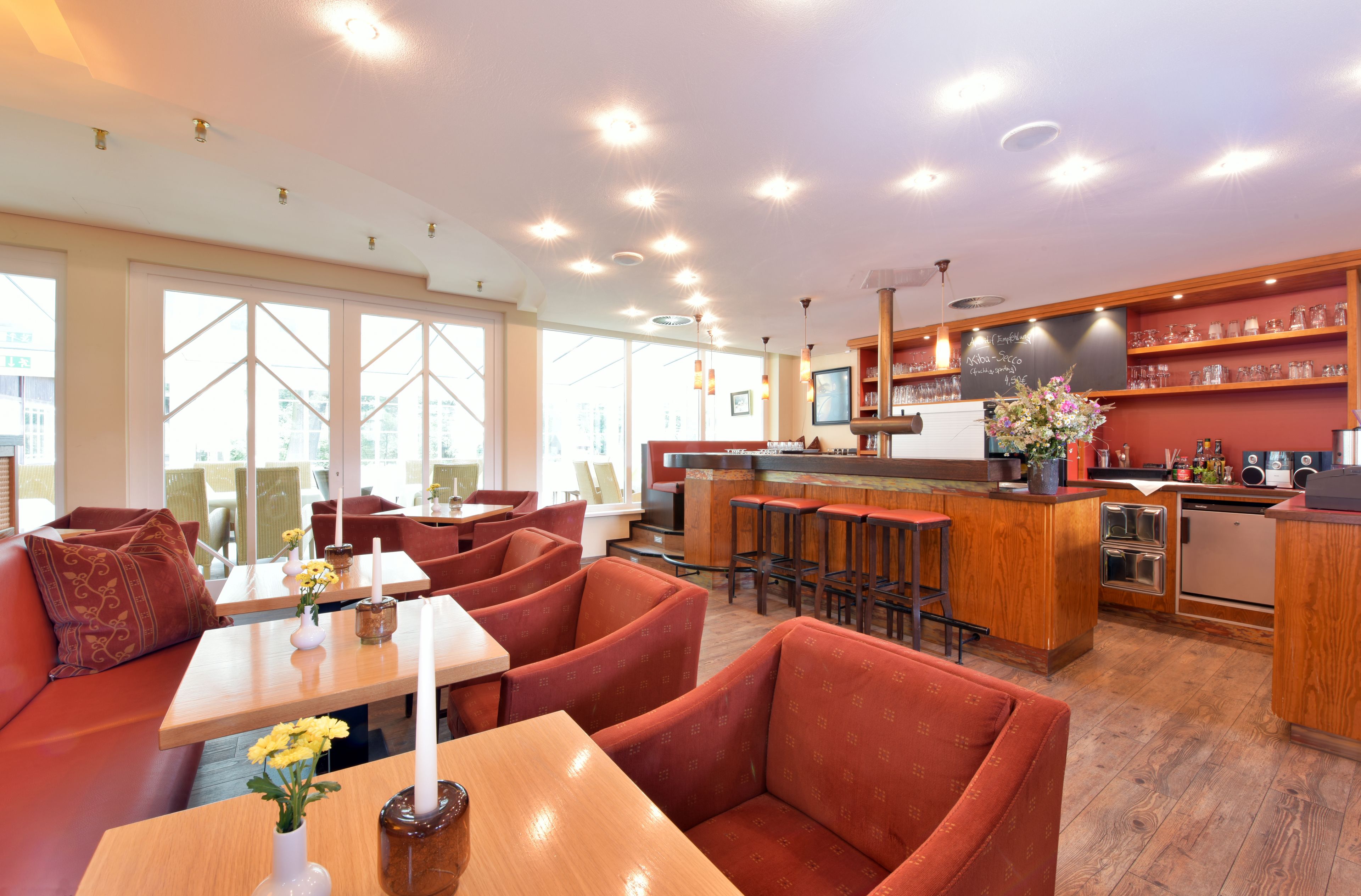 A modern restaurant with a bar area, seating with red upholstered chairs, and a view of the city through large windows.