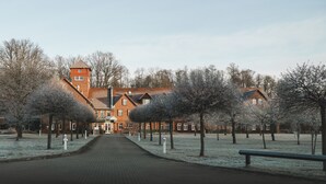 A brick building with a central tower, surrounded by trees and a paved pathway.