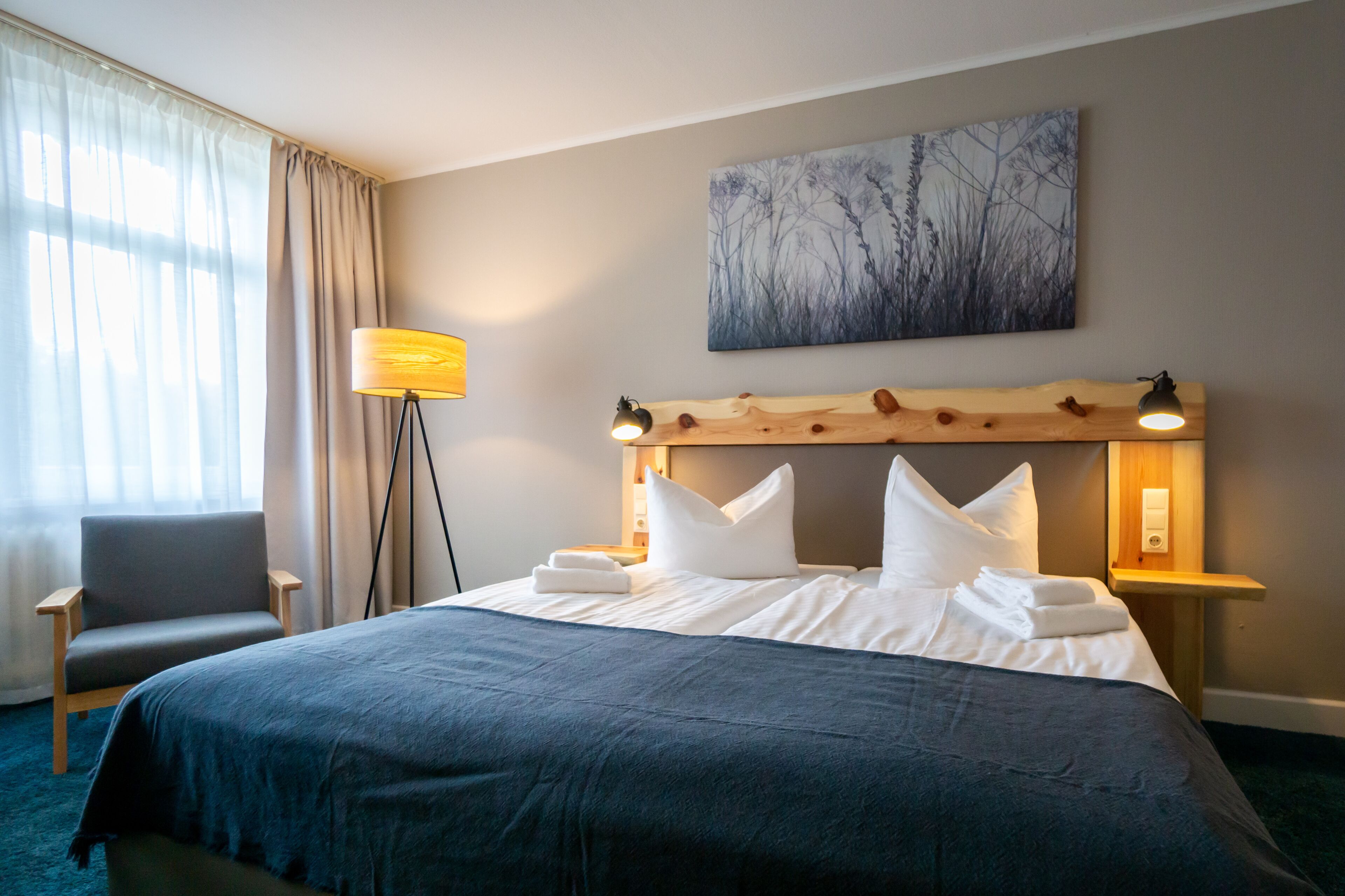 A neatly made bed with white linens, a wooden headboard, and a bedside lamp.
