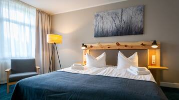 A neatly made bed with white linens, a wooden headboard, and a bedside lamp.