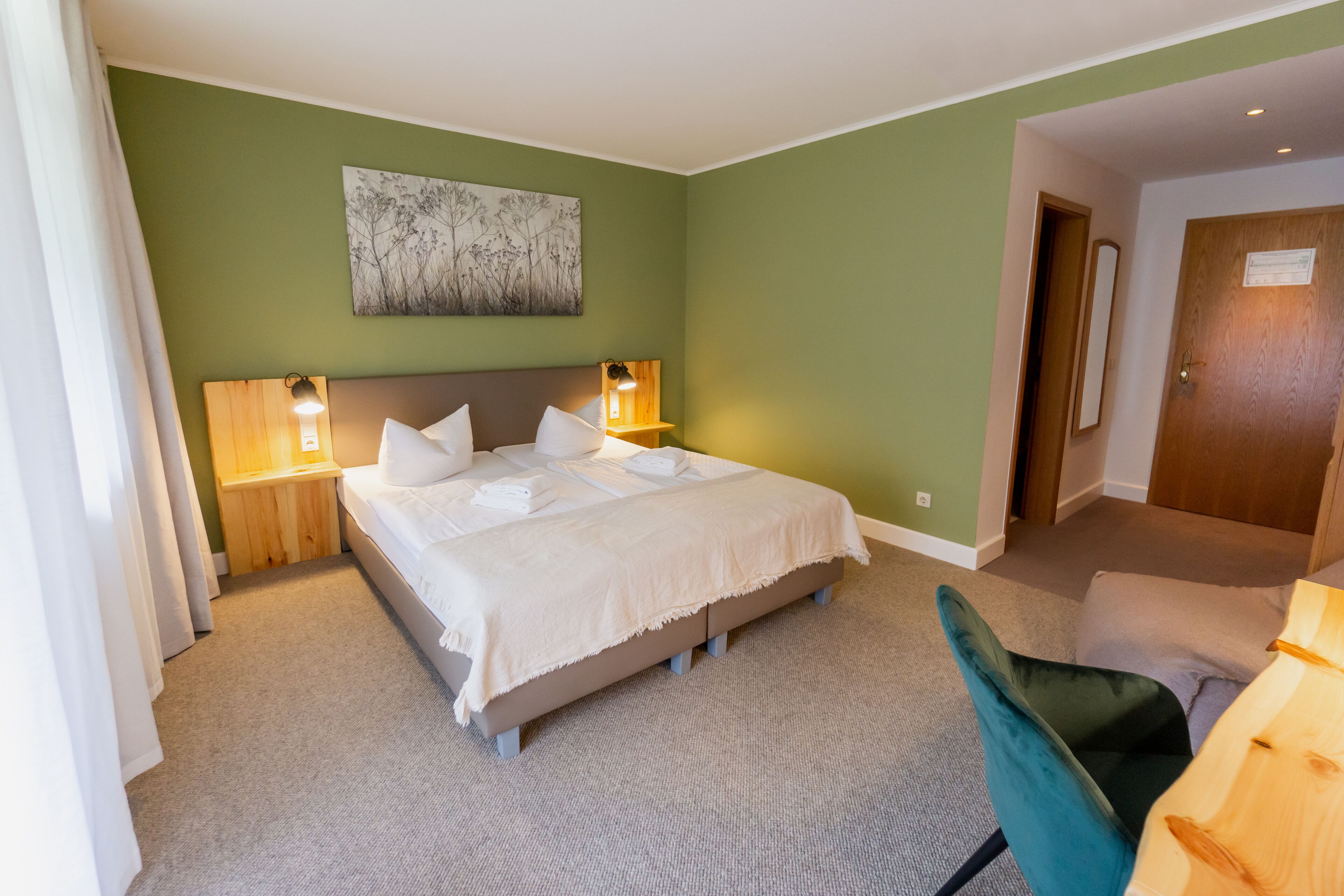 Habitación de hotel con una cama grande, lámparas de noche, un cabecero de madera, una pared de acento verde y una puerta a la derecha.