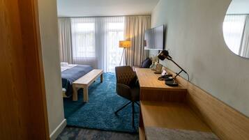 Ein Hotelzimmer mit Bett, Schreibtisch, Stuhl, Lampe und einem großen Spiegel.