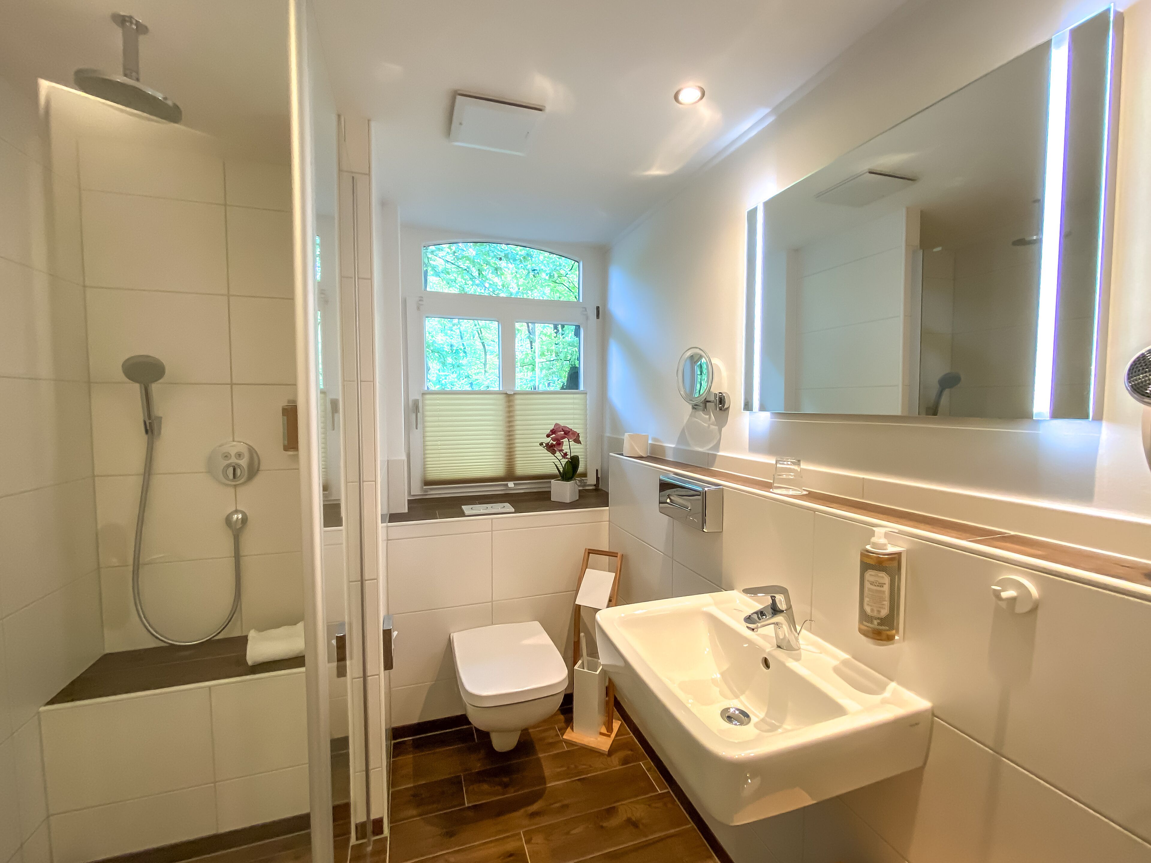Een moderne badkamer met douche, toilet, wastafel en een grote spiegel.