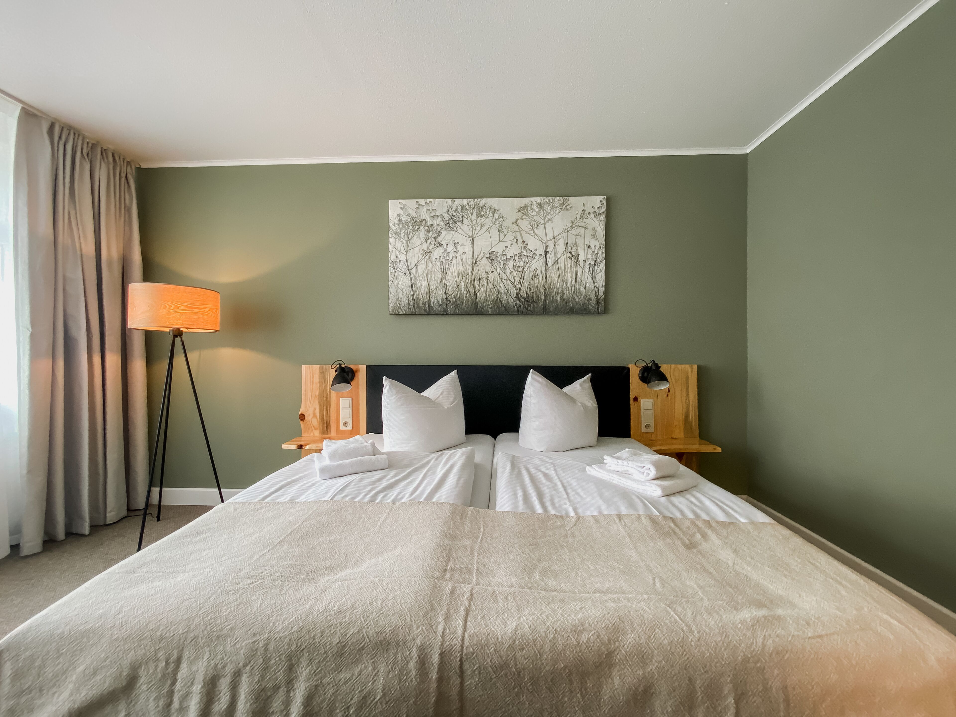 Una cama doble bien hecha con sábanas blancas, cabecera con panel oscuro y una obra de arte en la pared que representa una escena floral.