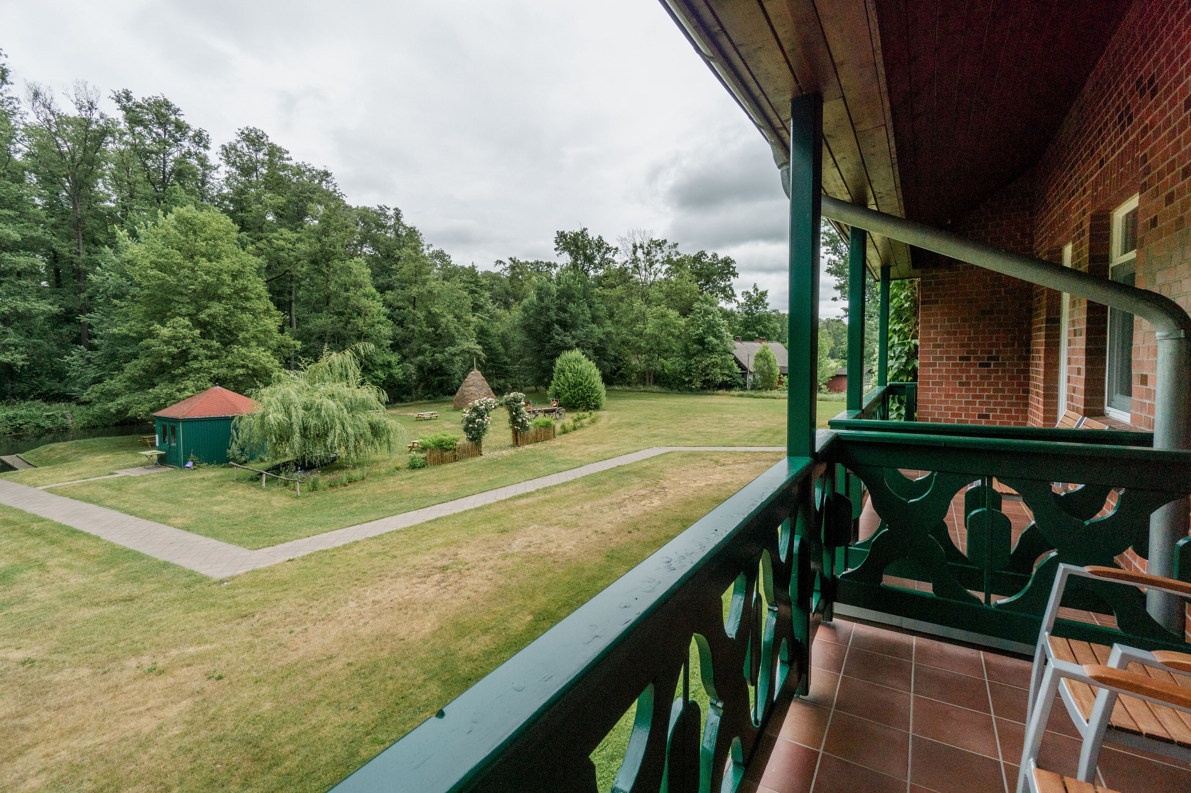 Un balcon donnant sur une cour verdoyante, un petit abri de jardin et un bâtiment en briques.