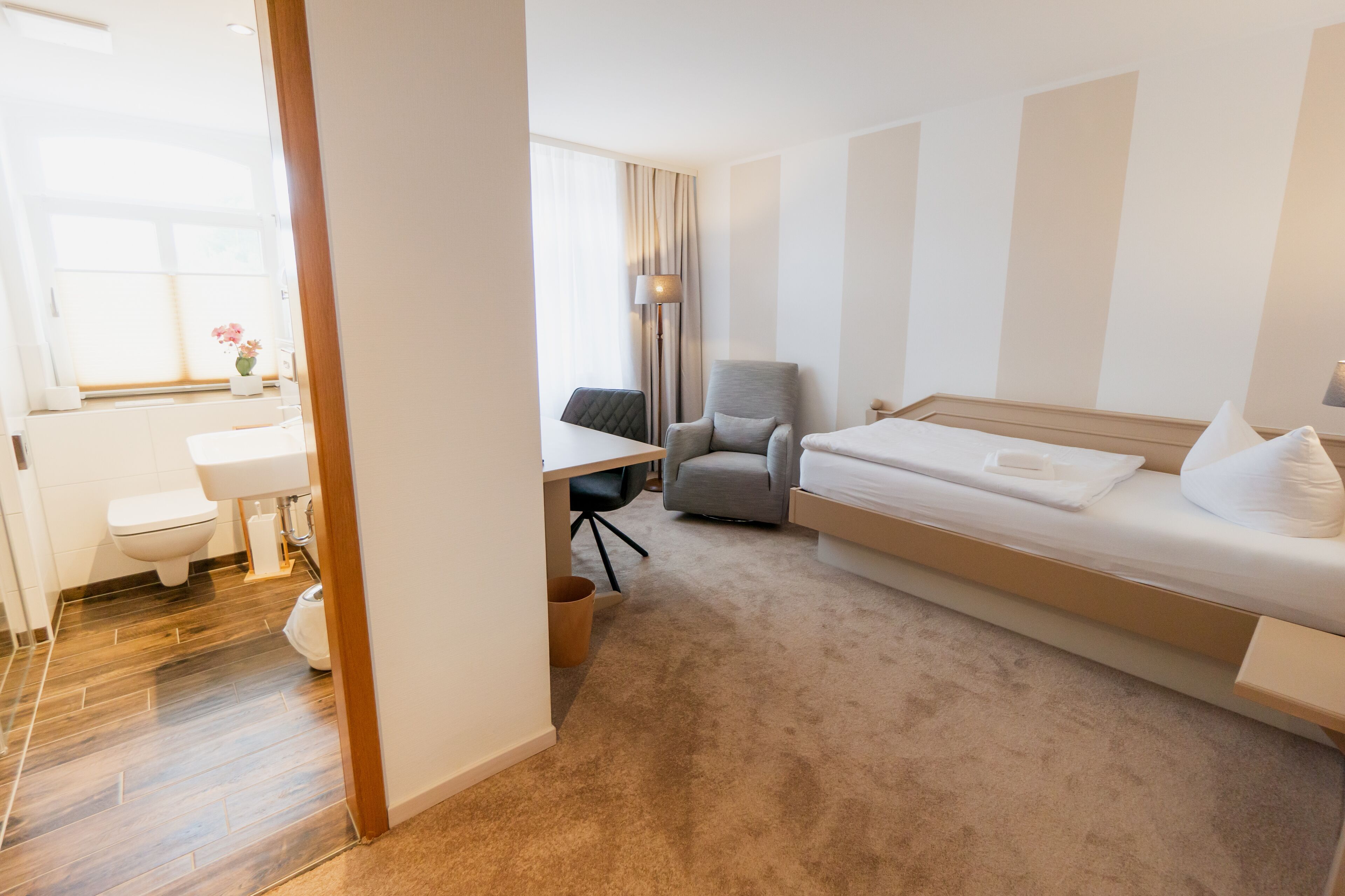 A hotel room with a bed, a desk, a chair, a toilet, and a sink.