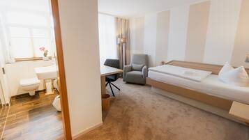 A hotel room with a bed, a desk, a chair, a toilet, and a sink.
