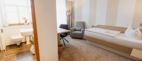 A hotel room with a bed, a desk, a chair, a toilet, and a sink.