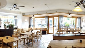 A restaurant with wooden tables and chairs, a bar area with bottles and glasses, and large windows with curtains. - Hotel Sörenberg (Fluehli)