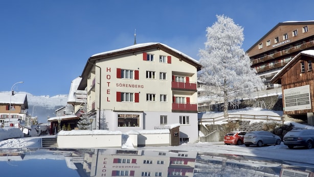 A hotel with a restaurant on the ground floor, a ski lift in the background, and a reflection in the water. - Hotel Sörenberg (Fluehli)