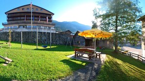 A hotel with a circular building, a stone wall, and a grassy area with a swing set. - Hotel Sörenberg (Fluehli)