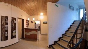 A hotel lobby with a reception desk, a staircase, and a curved wall with framed pictures. - Hotel Sörenberg (Fluehli)