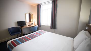 Habitación de hotel con una cama grande, un escritorio con computadora, una silla y una ventana con cortinas.