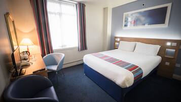 A hotel room with a bed, a desk with a computer, a chair, and a window with curtains.