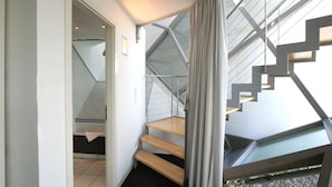 Un interno moderno con una scala che conduce a un balcone, una porta verso un'altra stanza e un pavimento piastrellato.