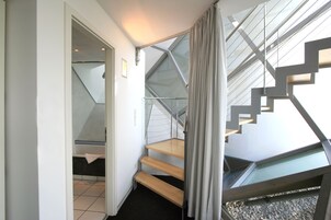 Un interior moderno con una escalera que lleva a un balcón, una puerta a otra habitación y piso de baldosas.