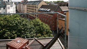 Una terrazza sul tetto con un tavolo e una sedia in legno, affacciata su un panorama urbano con edifici e alberi.