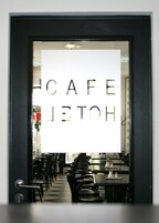 Un café con un letrero que dice "CAFE HOTEL" y vistas del área de mesas en el interior.