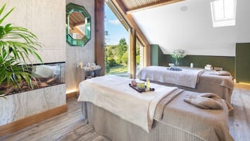 Relax in a serene spa room with two massage tables, a large mirror, and a potted plant.