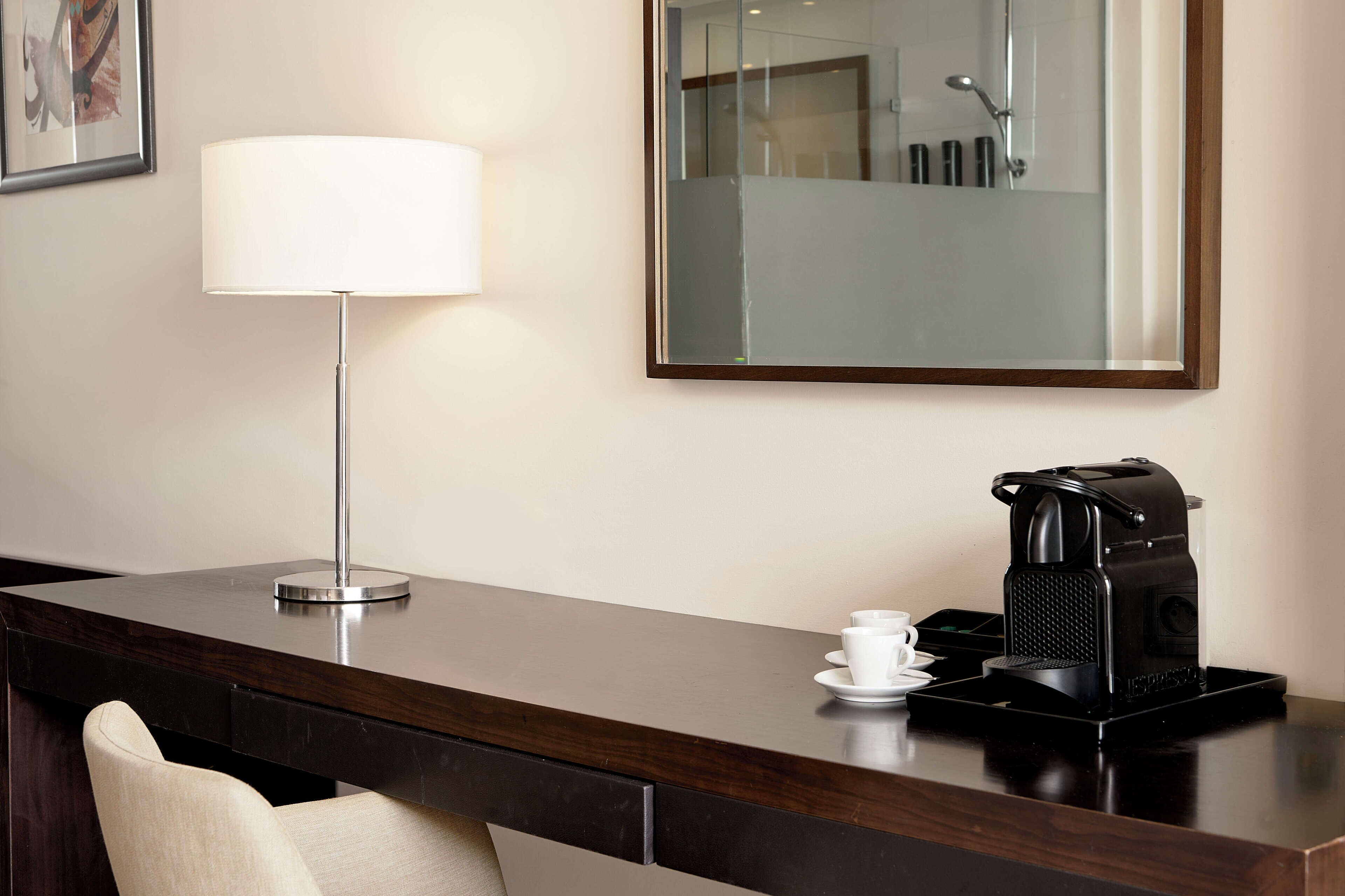 Ein Hotelrezeptionstresen mit einer Lampe, einer Kaffeemaschine und einem Spiegel, der ein Badezimmer reflektiert.